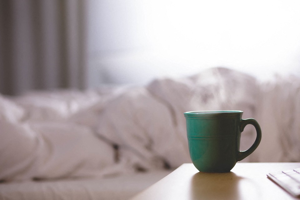 A mug with steam coming out of in front of bed with white linens
